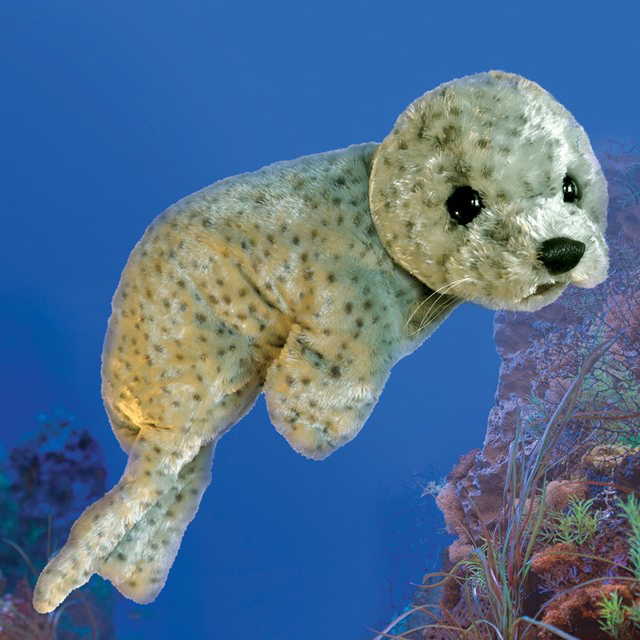 Folkmanis harbor seal baby hand puppet in light grey fur with dark spots, black glass eyes and whiskers, against a blue ocean background