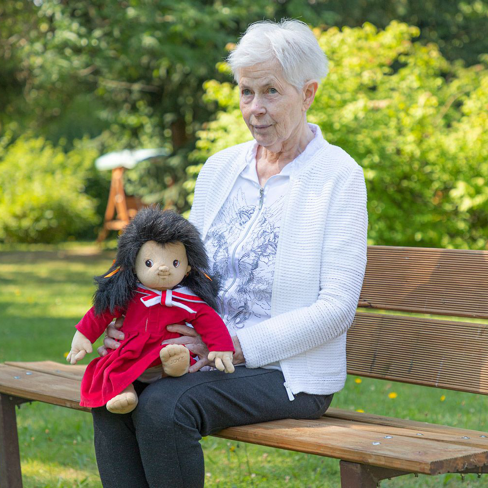 Senior lady with the Joyk empathy doll Mia on her lap on a garden bench