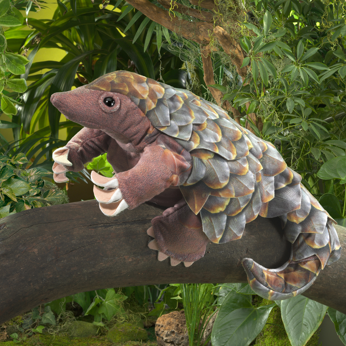 Folkmanis pangolin hand puppet with detailed grey scales and claws, perched on a branch in a tropical setting