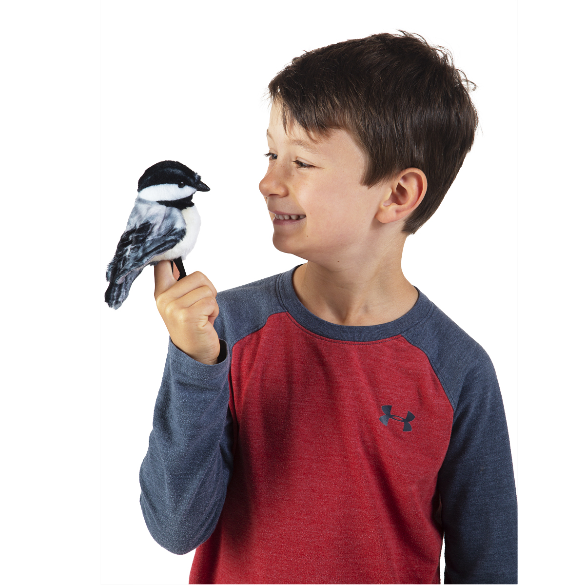 Boy holding a Folkmanis mini chickadee finger puppet with black-and-white plumage on his index finger, smiling at it