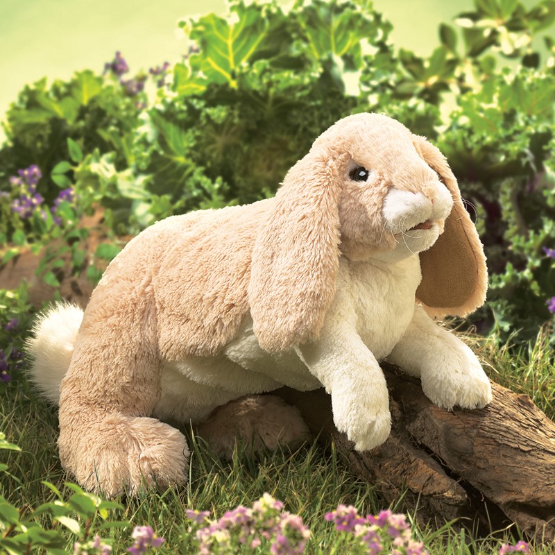 Folkmanis hand puppet cuddly bunny with light beige plush fur and long floppy ears, lying on a log in the grass