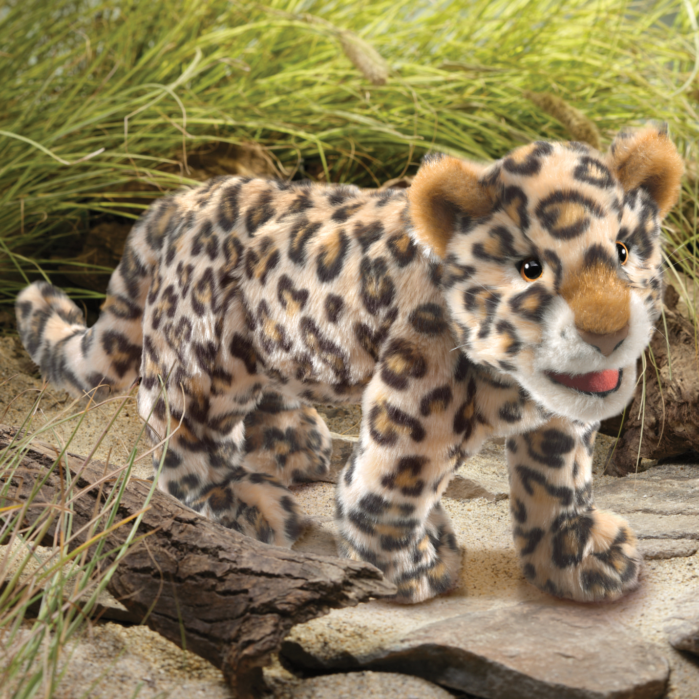 Folkmanis leopard cub hand puppet with beige spotted fur, orange ears and open mouth, standing on stones in front of grass