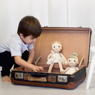 Child discovering two Rubens EcoBuds dolls in a vintage suitcase