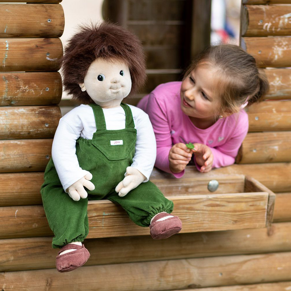 The Joyk empathy doll Marco sitting at a playhouse window next to a child