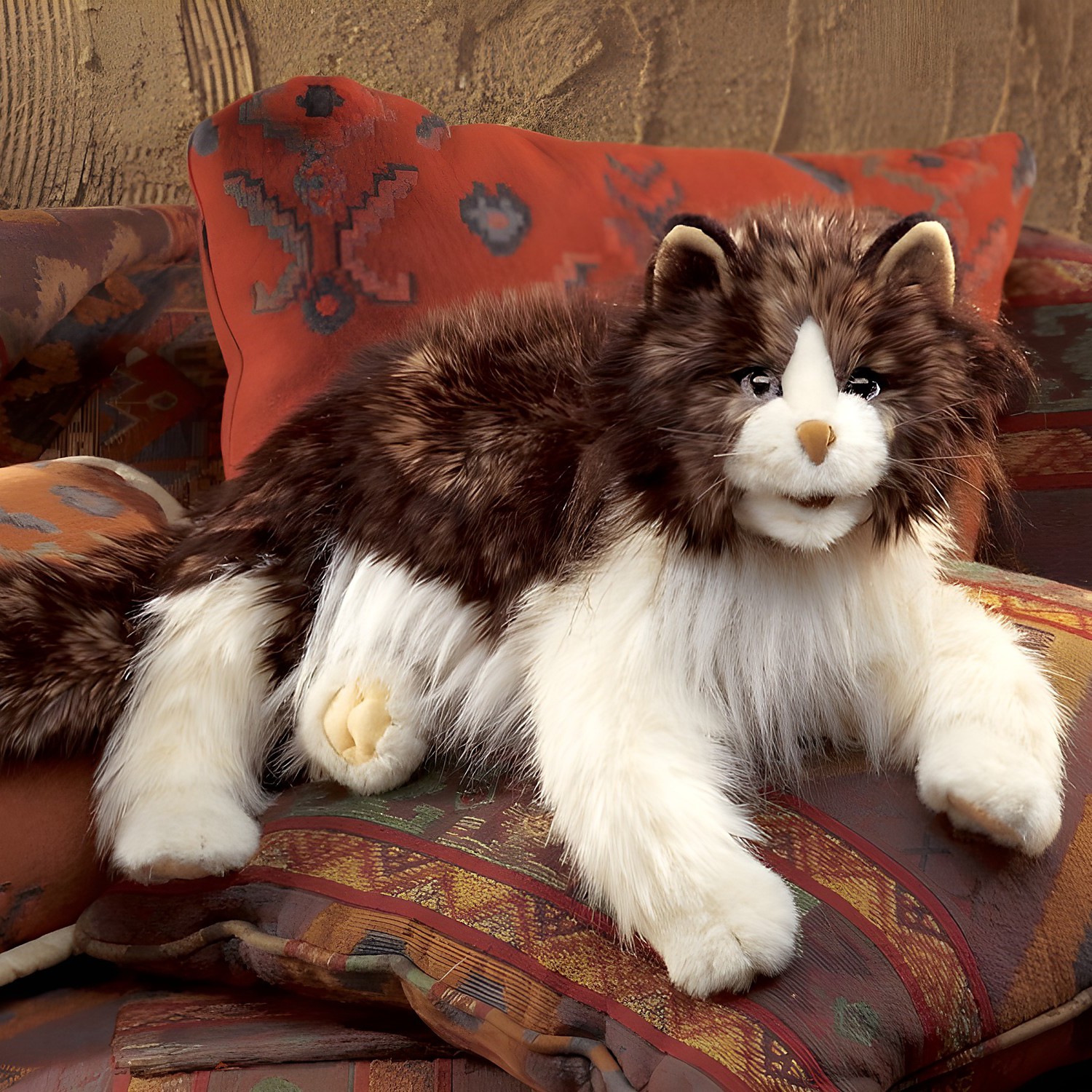 Folkmanis hand puppet fluffy cat with brown-and-white long fur, lying on patterned cushions, side view