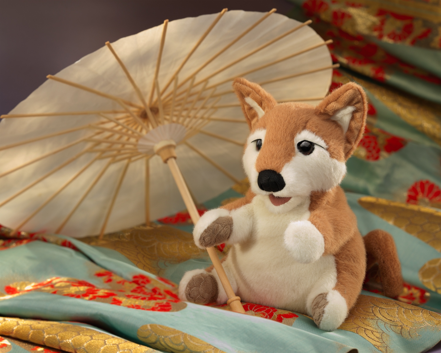 Folkmanis Shiba Inu hand puppet in brown and white, sitting and holding a paper parasol, on embroidered silk fabrics in gold and teal