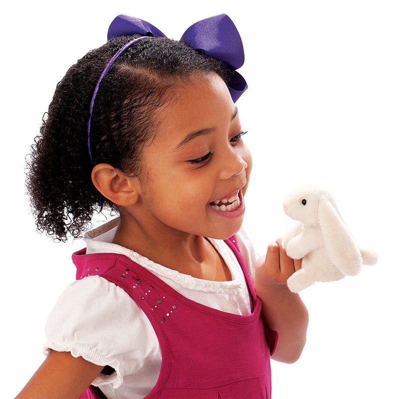 Girl with a purple hair bow laughing while playing with the white Folkmanis mini lop-eared rabbit finger puppet on her index finger