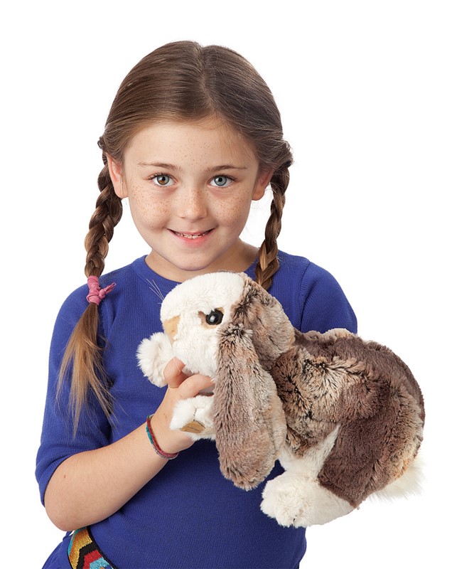 Girl holding a Folkmanis baby lop rabbit hand puppet with brown-and-white fur and long floppy ears towards the camera