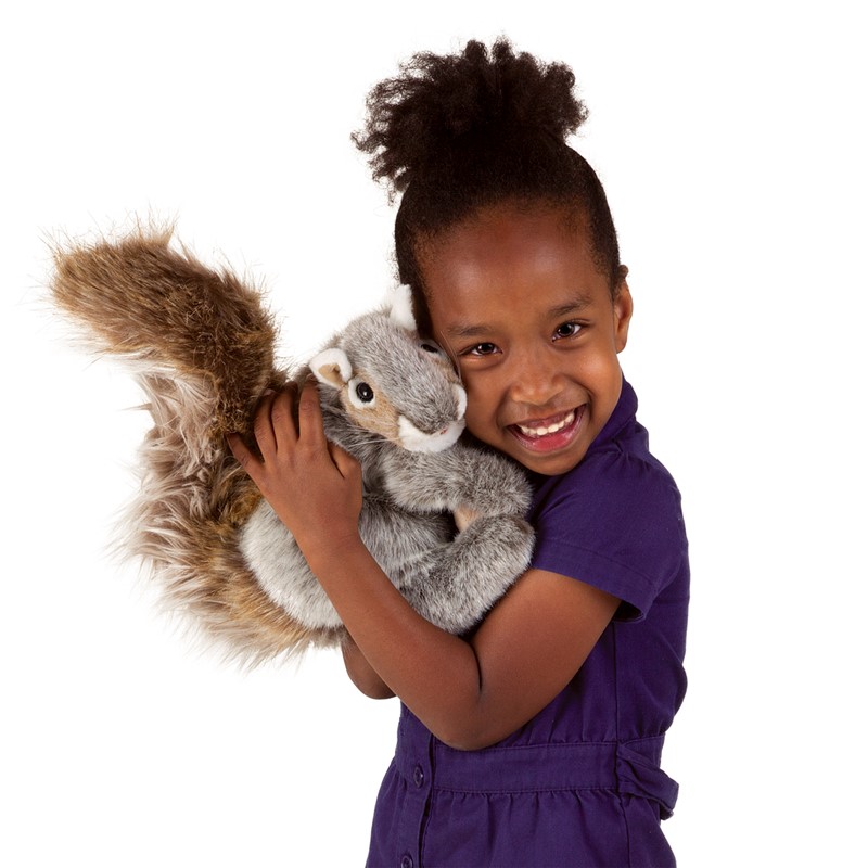 Girl smiling and holding a Folkmanis grey squirrel hand puppet with a bushy brown tail against her cheek