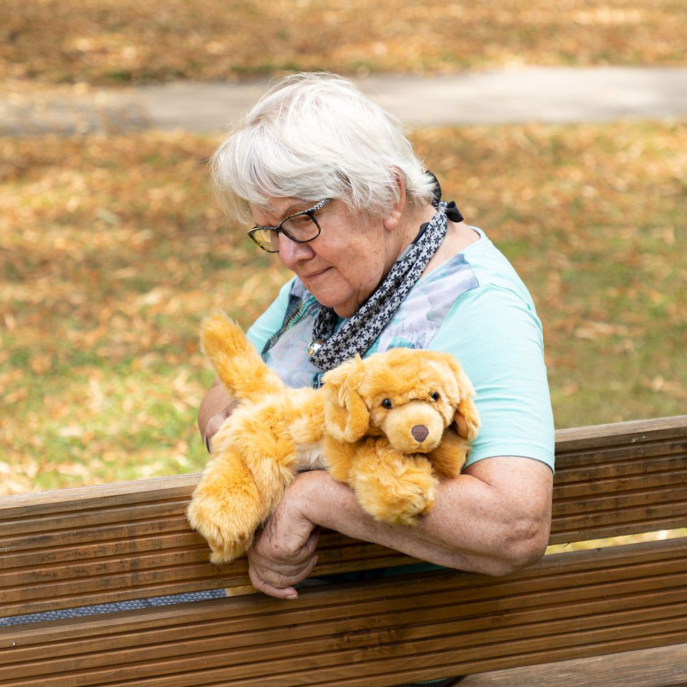 Senior lady holding the Joyk empathy doll Brando in her arms on a park bench