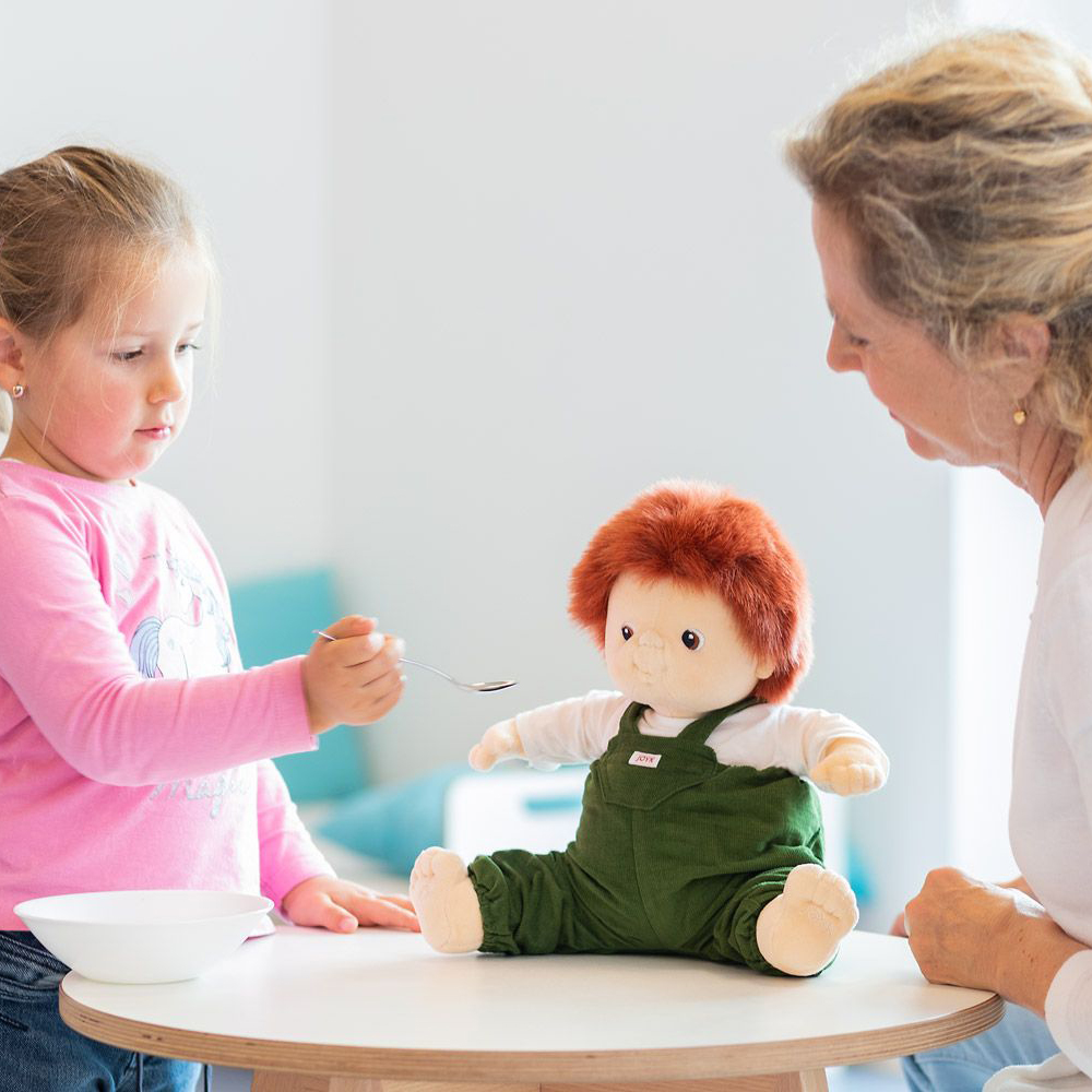 Child feeding the Joyk empathy doll Sam at the table with a spoon