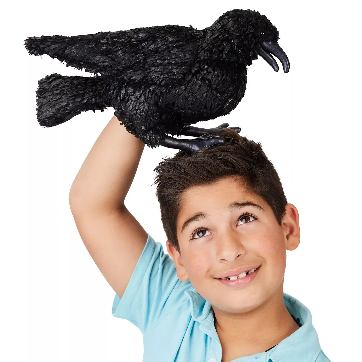 Boy holding a Folkmanis crow hand puppet with black plumage and claws above his head, smiling up at it