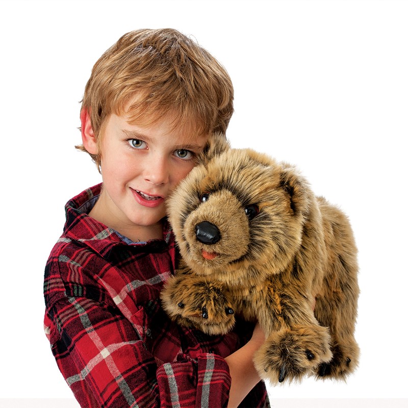 Boy holding a Folkmanis grizzly bear hand puppet with brown plush fur and a black nose in his arms