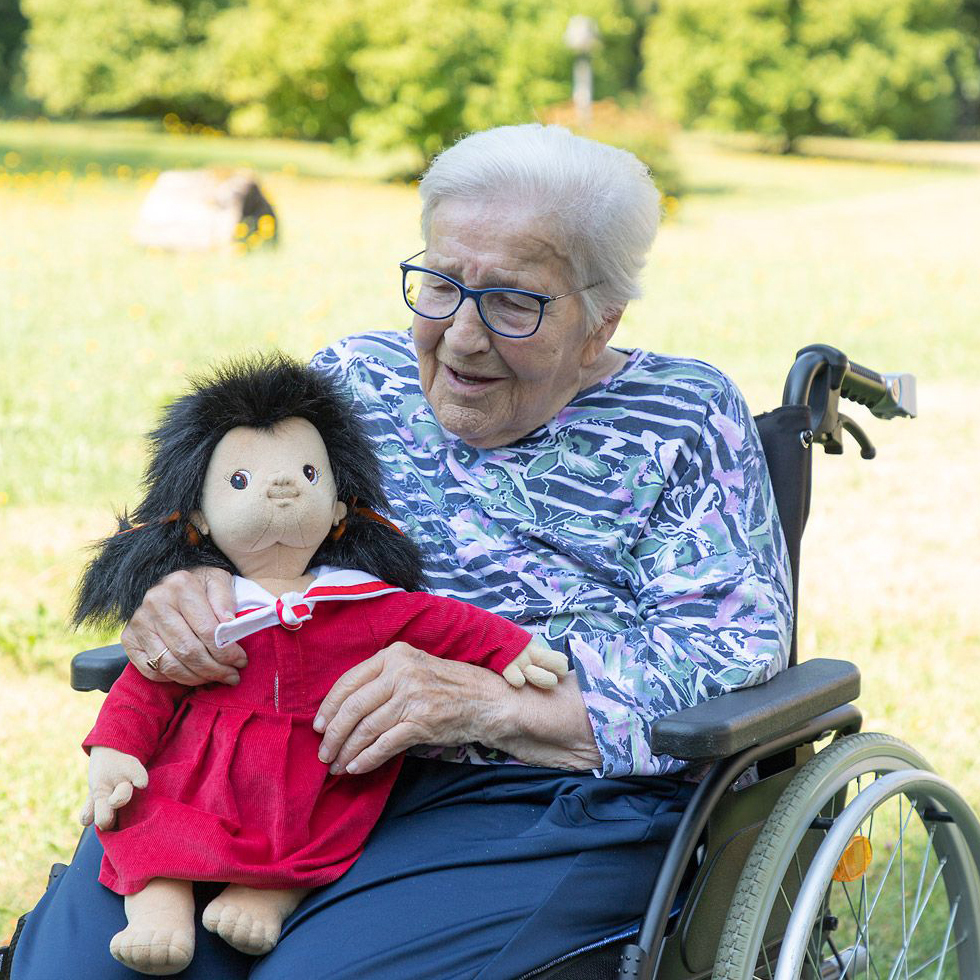 Senior lady in a wheelchair holding the Joyk empathy doll Mia in her arms
