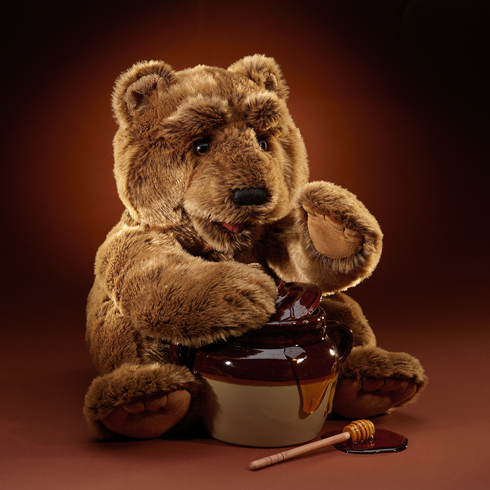 Folkmanis large bear hand puppet sitting beside a honey pot, mouth open with one paw reaching towards it.