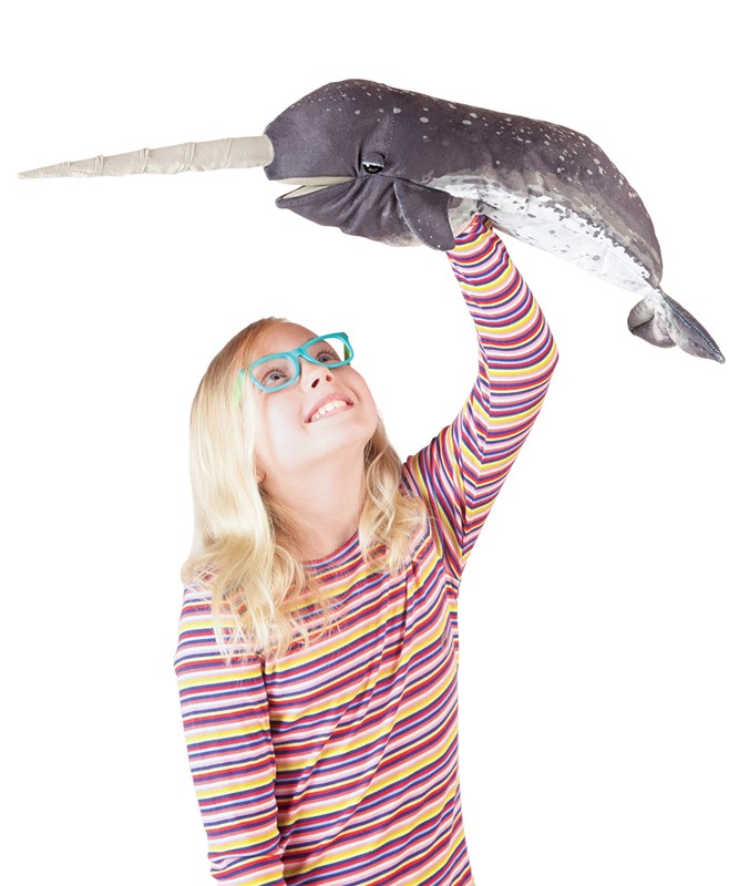 Girl holding a Folkmanis narwhal hand puppet with realistic fur print and long horn high above her head