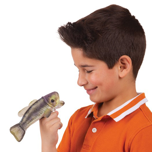 Boy in an orange polo shirt holding a Folkmanis mini largemouth bass finger puppet on his finger and smiling at it