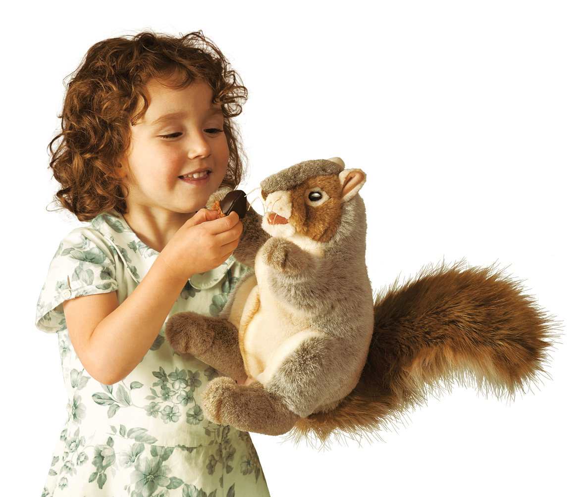 Girl holding a Folkmanis grey squirrel hand puppet with a bushy tail and offering it an acorn