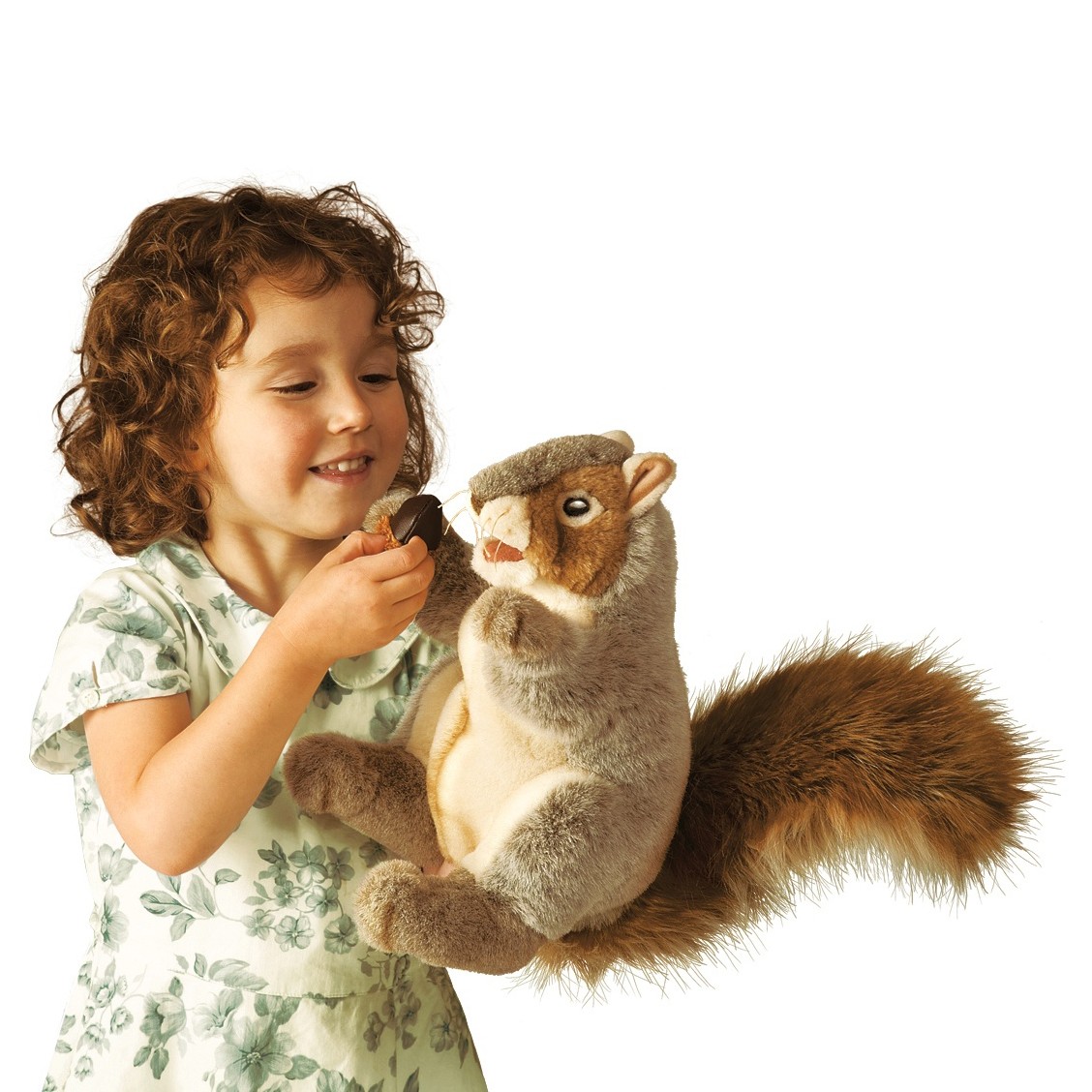 Girl holding a Folkmanis grey squirrel hand puppet with a bushy tail and offering it an acorn