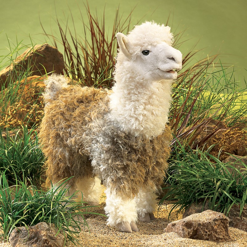 Folkmanis alpaca hand puppet with curly white and beige fur in a standing pose in front of a green nature diorama