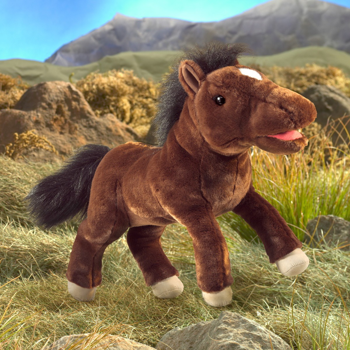 Folkmanis horse hand puppet in dark brown with a black mane, white forehead spot and movable mouth, side view against a mountain backdrop