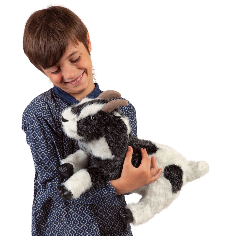 Boy smiling while holding the Folkmanis goat hand puppet with black-and-white fur and brown horns in his arms