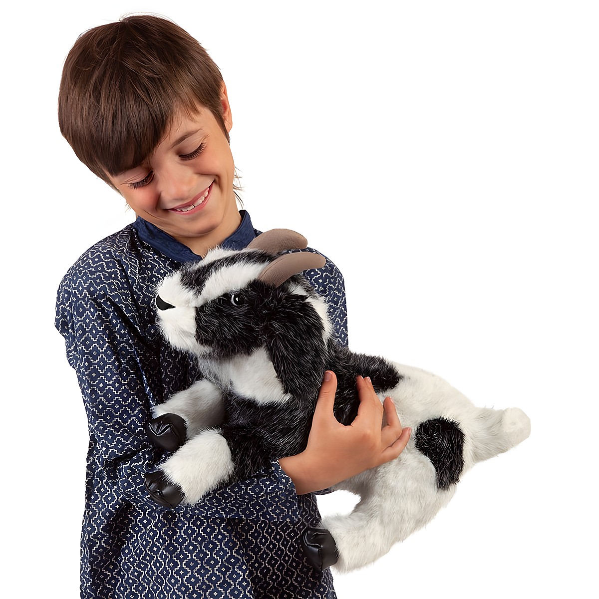 Boy smiling while holding the Folkmanis goat hand puppet with black-and-white fur and brown horns in his arms
