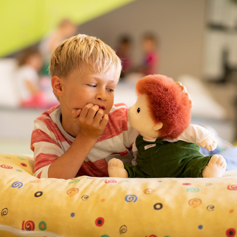 Child making eye contact with the Joyk empathy doll Sam on a cushion