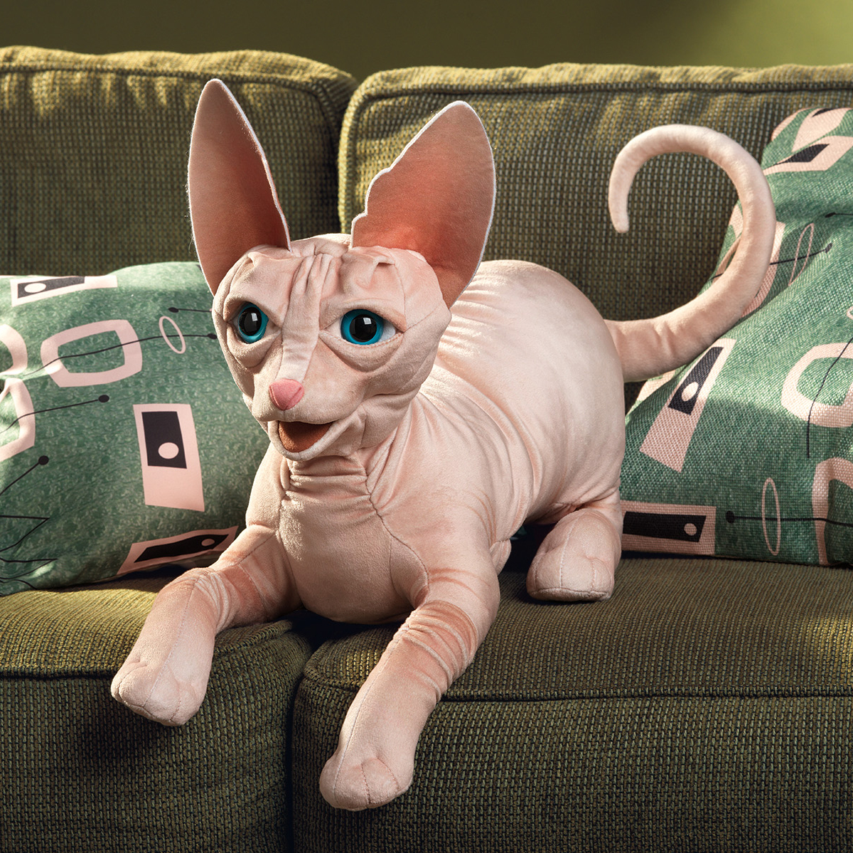 Folkmanis hand puppet Sphynx cat in pink-beige with turquoise eyes and large ears, lying on a green sofa