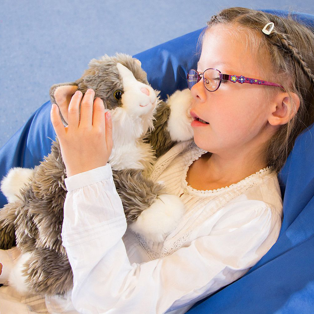 Child holding the Joyk empathy doll Billy, a grey-white plush cat, in their arms