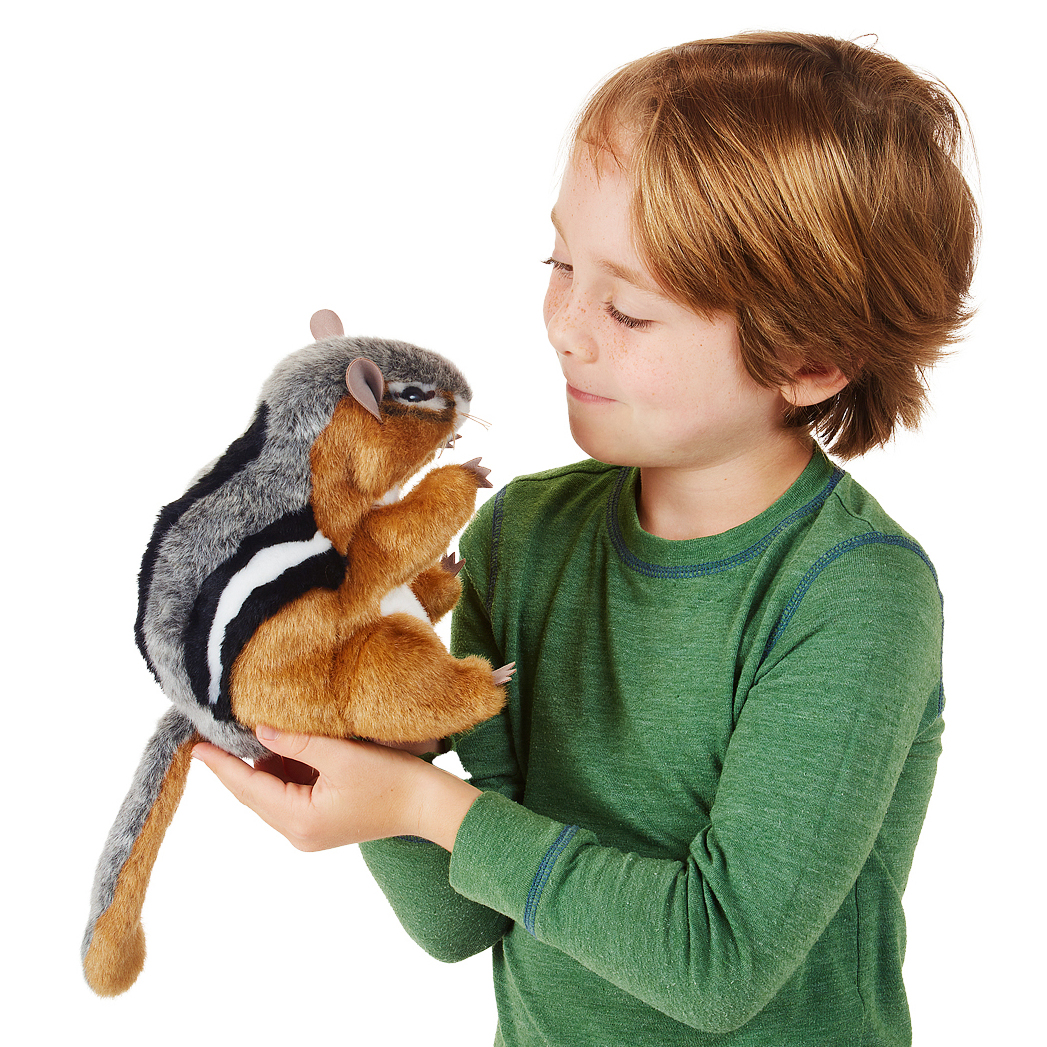 Boy holding the Folkmanis chipmunk hand puppet with brown, grey and black striped fur in both hands, smiling at it