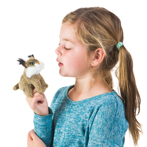 Girl wearing a Folkmanis mini bobcat finger puppet on her index finger and blowing on the small plush figure