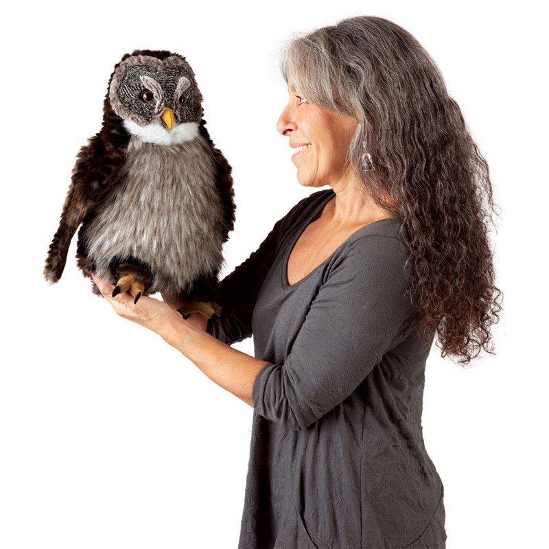 Woman holding a Folkmanis owl hand puppet with brown plumage, grey belly and yellow beak on her flat hand, side view