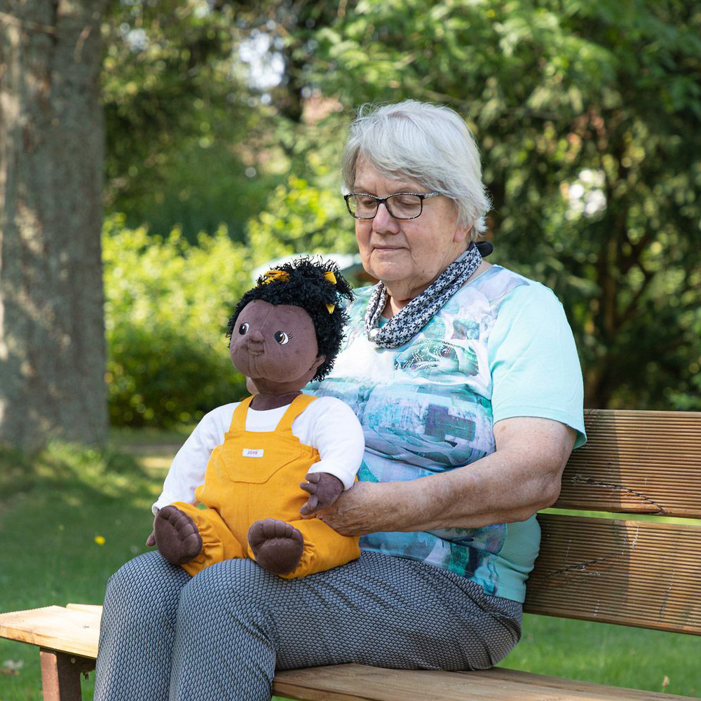 Senior lady sitting with the Joyk empathy doll Sofia on a garden bench