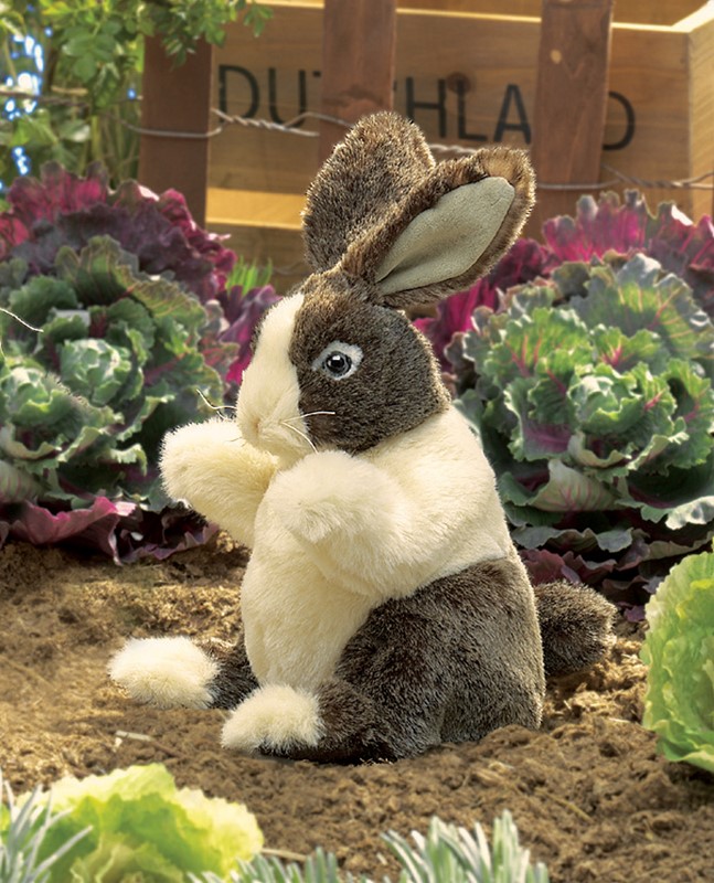 Folkmanis hand puppet baby Dutch rabbit with brown head and white body, sitting upright in a vegetable bed