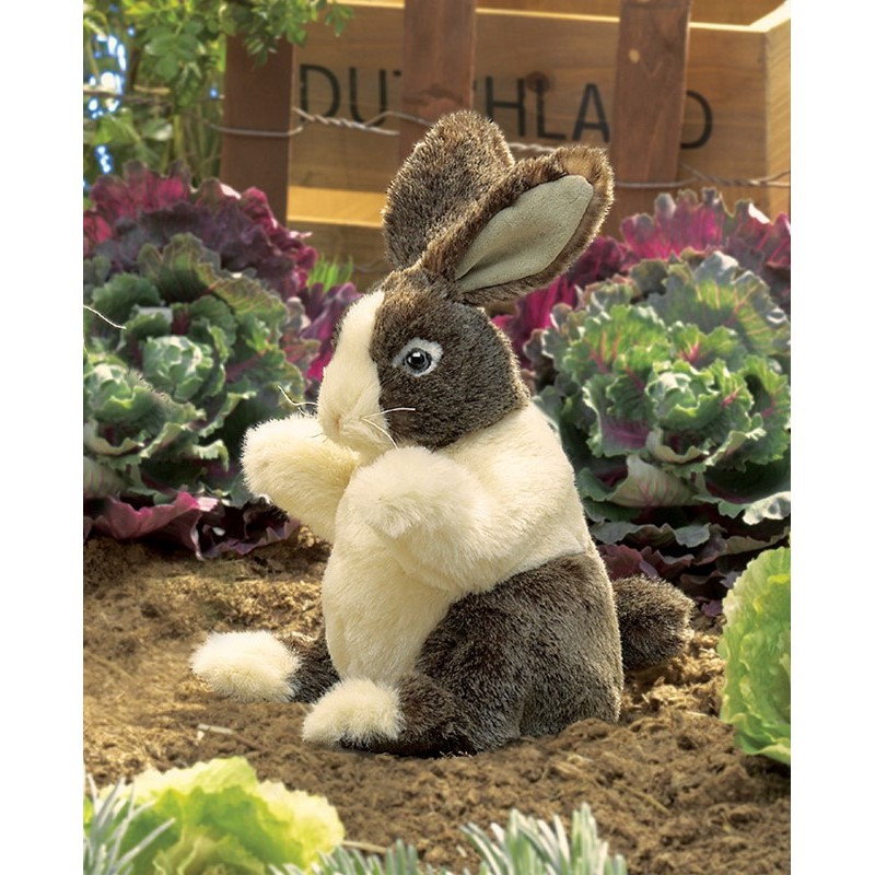 Folkmanis hand puppet baby Dutch rabbit with brown head and white body, sitting upright in a vegetable bed