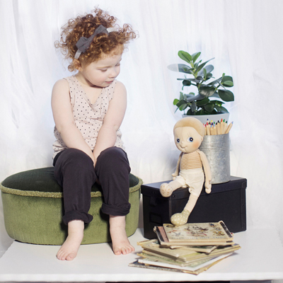 Child looking at the Rubens EcoBuds doll Aspen on a wooden box