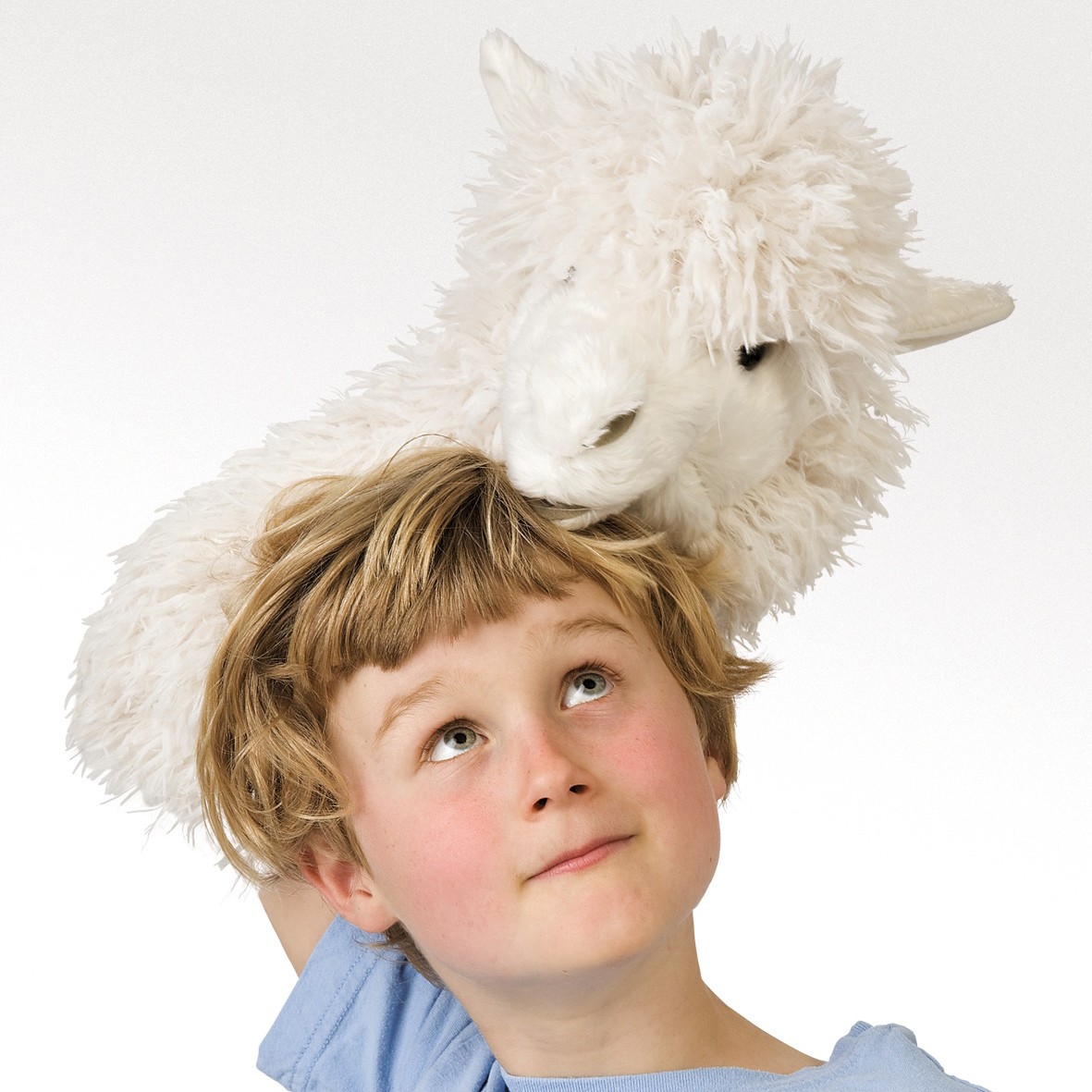 Child balancing a white Folkmanis alpaca hand puppet with shaggy fur on their head, looking up with a smile