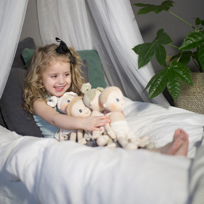 Child laughing and pointing at the Rubens EcoBuds dolls on the bed