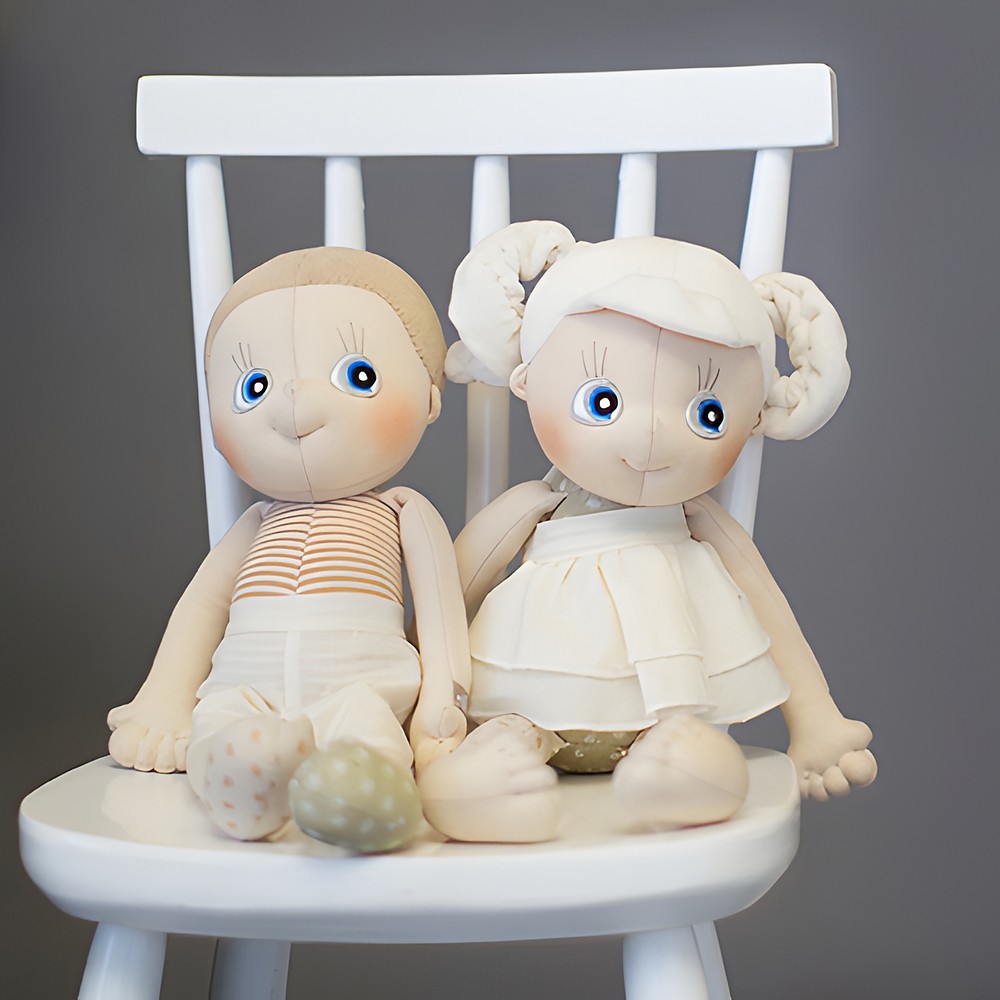 Two Rubens EcoBuds dolls sitting next to each other on a white children's chair