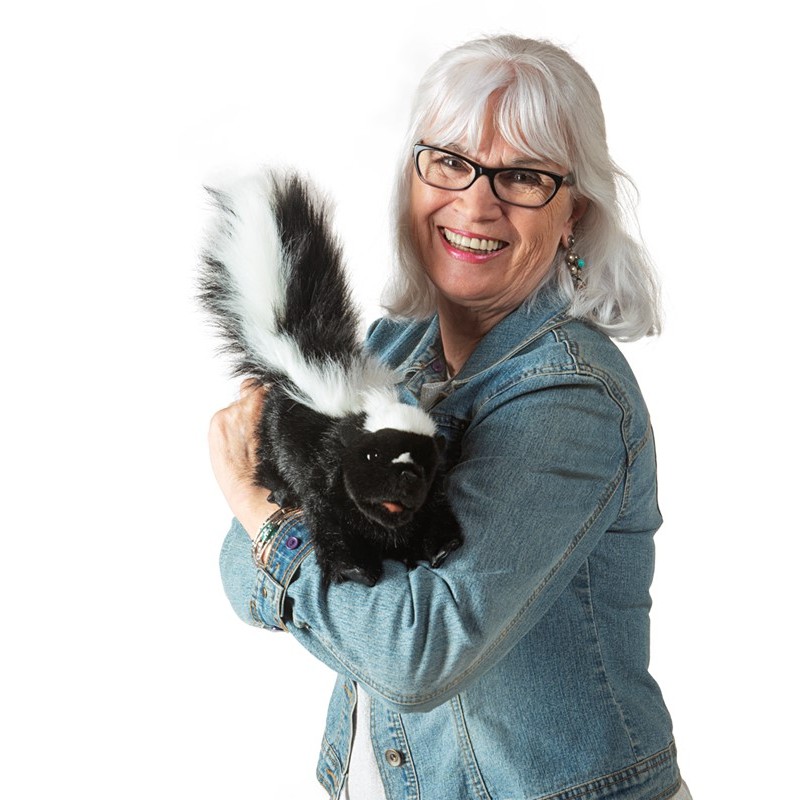 Smiling woman holding the Folkmanis skunk hand puppet with black-and-white fur and a bushy tail in her arms