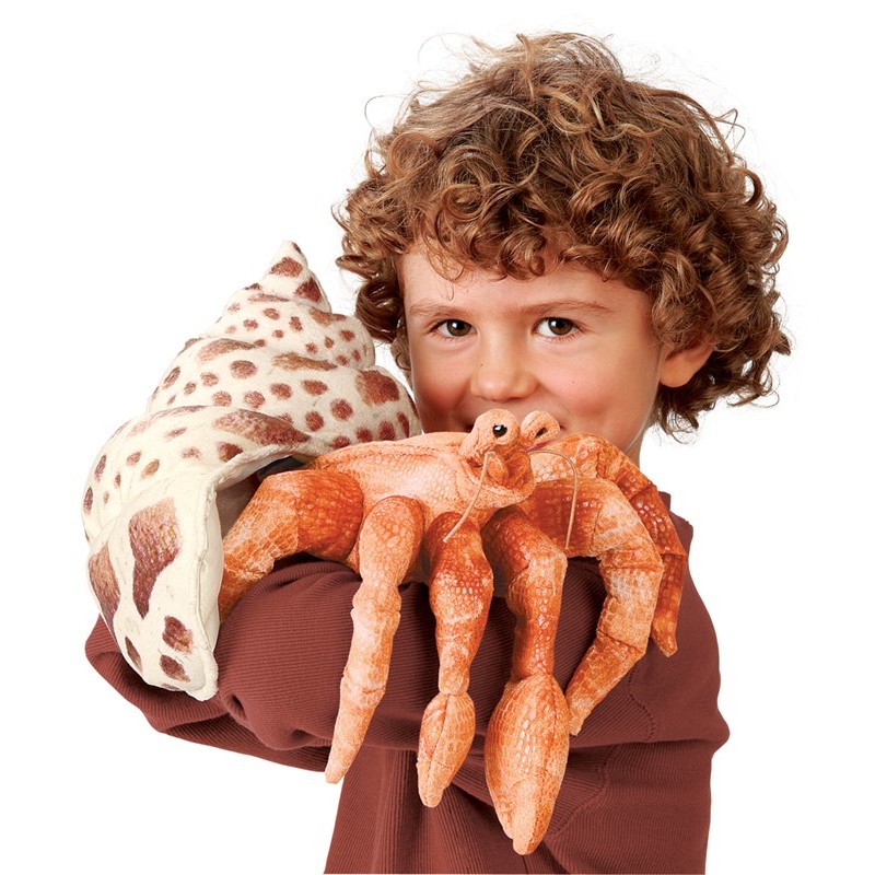 Folkmanis hermit crab hand puppet in orange with a spotted snail shell, held towards the camera by a child