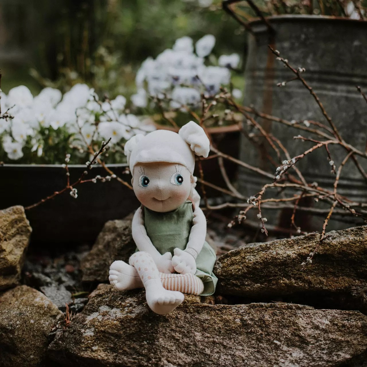 Rubens EcoBuds doll in the green spring outfit sitting on a garden wall