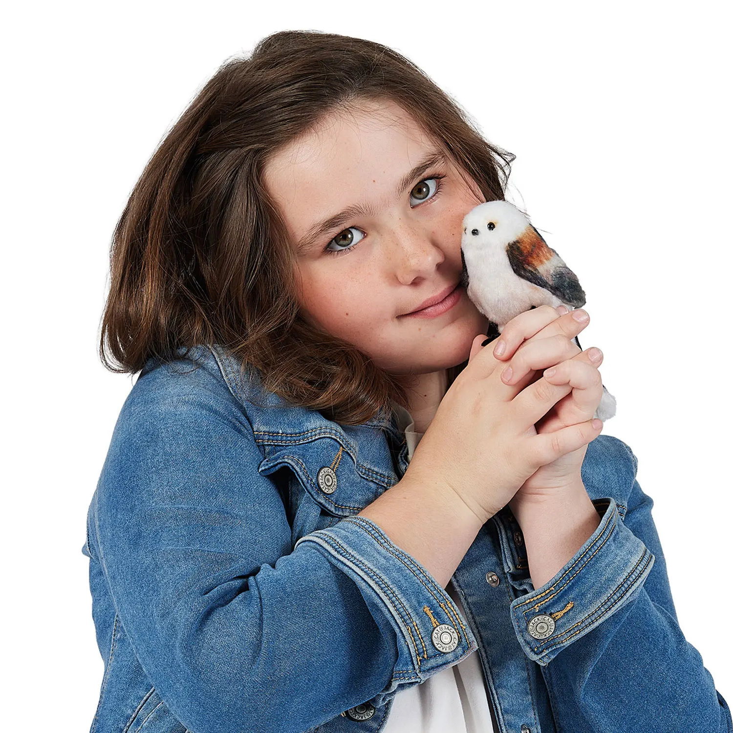 Girl holding a tiny Folkmanis long-tailed tit finger puppet with white plumage and brown wings against her cheek
