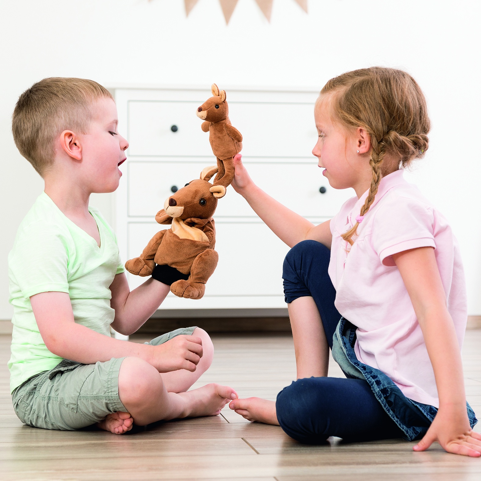 Two children facing each other playing with the Beleduc story hand puppet kangaroo Kanga, usage example