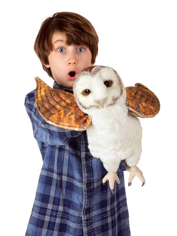 Boy holding a Folkmanis barn owl hand puppet with spread wings and white plumage towards the camera