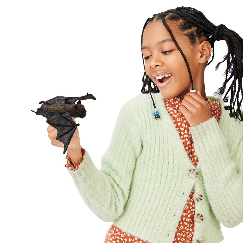 Girl holding a Folkmanis mini bat finger puppet in black with spread wings on her finger and laughing