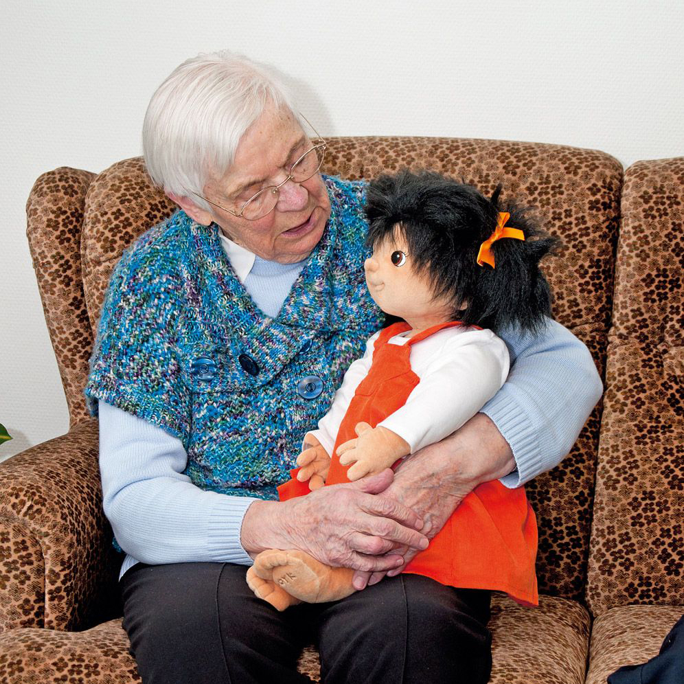 Senior lady with the Joyk empathy doll Emelie on her lap in an armchair