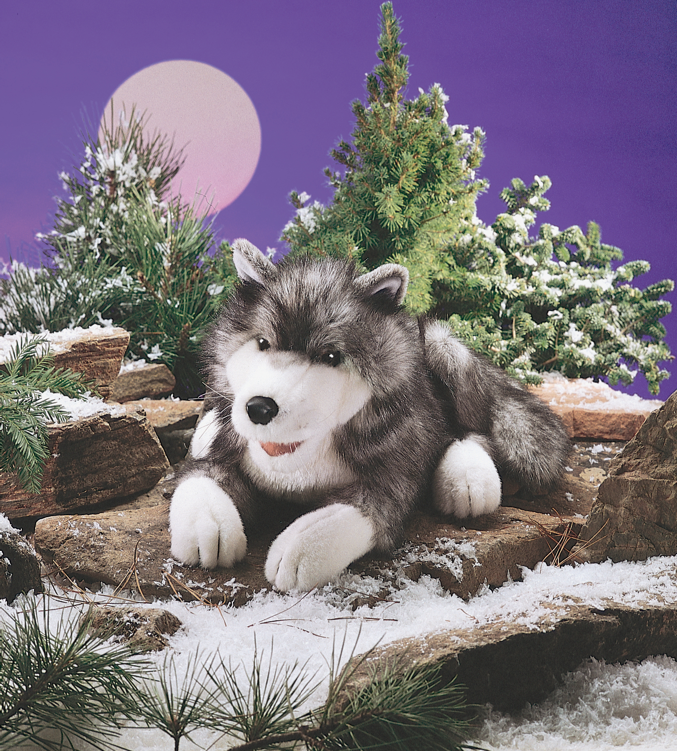 Folkmanis hand puppet timber wolf in grey and white, lying on rocks against a snowy winter backdrop with a moon disc