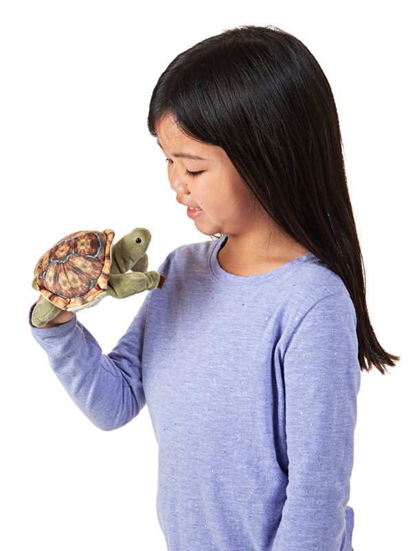 Girl wearing a Folkmanis mini tortoise finger puppet with a patterned shell on her hand, side view